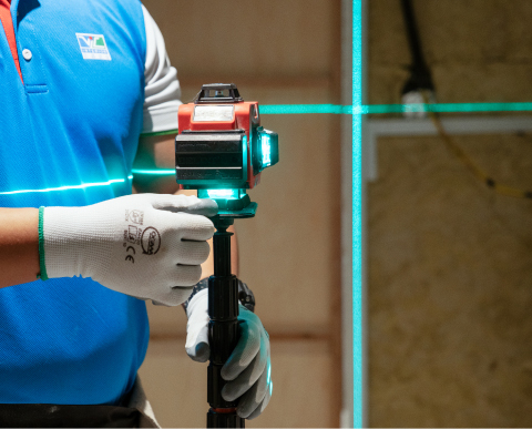 Worker using precision laser equipment to ensure adherence to quality control and assurance standards in construction projects